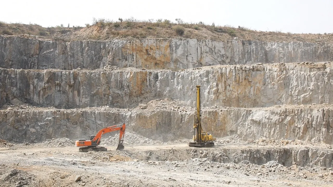 Benched quarry face at a Fortune mine, with a drill rig and excavator working the lower bench
